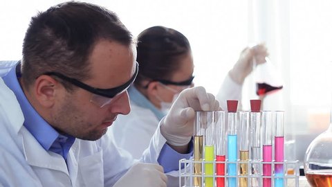Scientist looking at test tube with colorful liquid, female coworker in background