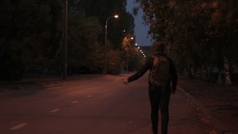 Man in summer night, with a backpack goes on road hitch-hike