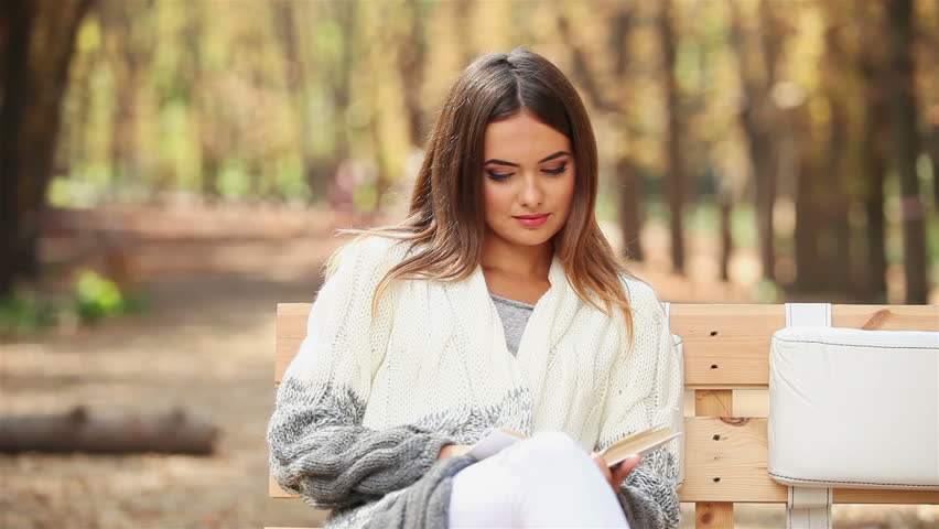 Attractive young woman reading a book in the park on an autumn day 