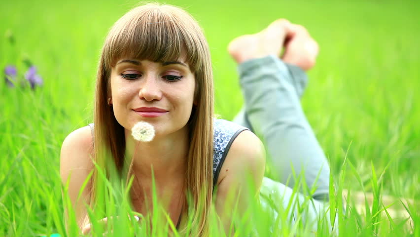 Young woman lying on the grass and blowing a dandelion