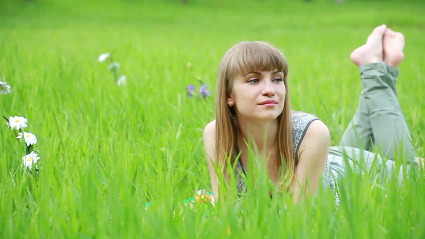 Young woman lying on grass and smiles. Looks at camera. Tripod.