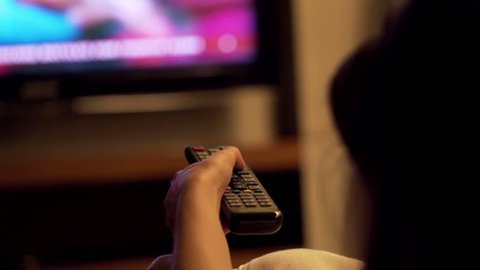 Woman watching TV at night and changing channels with remote
