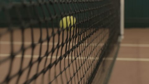 Yellow-green tennis ball stuck in the grid on red clay courts. Small depth of field