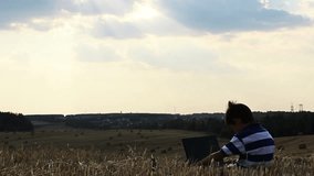 boy with a laptop in a field at sunset, boy working on a laptop at sunset on top, beautiful sky, beautiful clouds - Powered by Shutterstock - Get 15% off with code: PIKWIZARD15
