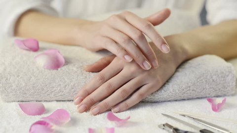 Closeup shot of female hands with french manicure on a towel surrounded by petals and manicure set. Woman getting nail manicure. Shallow depth of field with focus on woman hand.