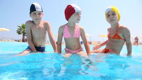 The boy and two girls sitting in the pool, girl pushed boy and then boy pushed girl 