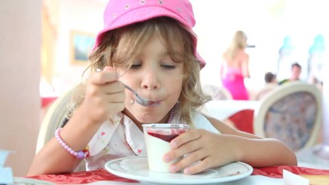 A little girl with curly hair and a pink hat, ate yogurt with jam 