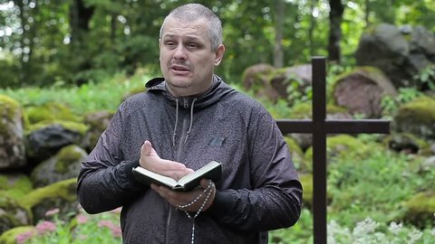 Preacher with Bible and rosary at outdoors church near cross