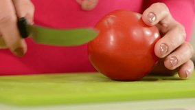 Woman with a knife cutting a tomato, hands close up.