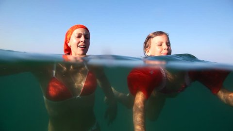Mom and daughter swimming in the sea, the camera goes under water, shown as they float 