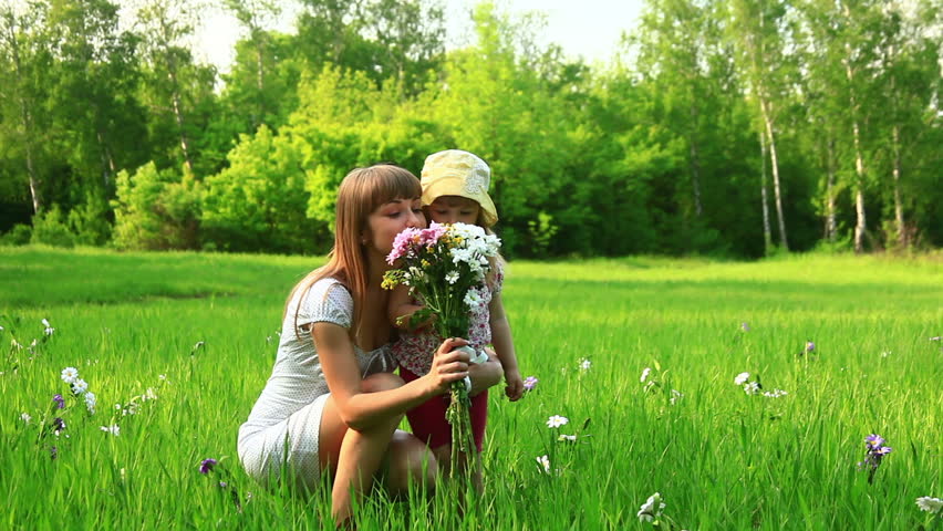 Young mother and child with flowers in the field. Look at Camera-1. Dolly 