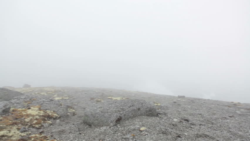 Descent from the mountain blocked with rainy mist cloud, hiker waiting the wind at steep slope. Khibiny massif, Kola peninsula, Russia