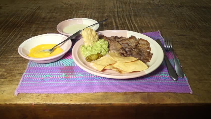 Nachos served with real melted cheese, sour cream, guacamole, chile and steak on a dish over a typical Mexican table top over a wood table. Steak on the foreground of the dish. Close Up. 