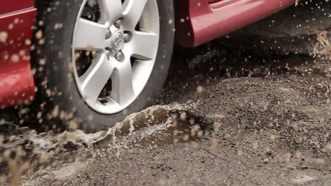 Car Hits Two Pot Holes. slow motion of a car driving through two potholes filled with water. splashing everywhere.