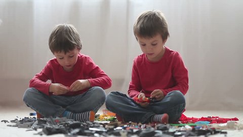Little children playing with lots of colorful plastic blocks indoor, building a fire truck and a fire house, reading from a manual and imagining