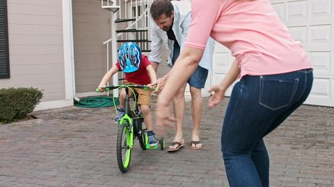 4k shot of father teaching son how to ride his bike and mother guiding her son on their home driveway with safety helmet. 