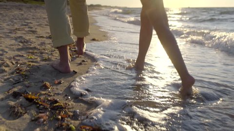 Couple Walk Along Beach, Closeup Of Legs/Bare Feet, Waves Crash At Their Feet