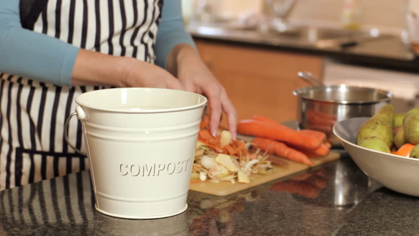 Woman recycles vegetable peelings by putting them into a compost caddy