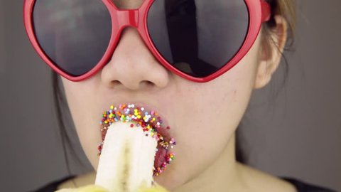Sexy woman with glasses eating banana with colored sugar.