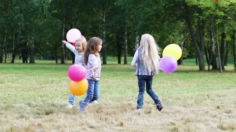 Three girls having fun running in the park with balloons