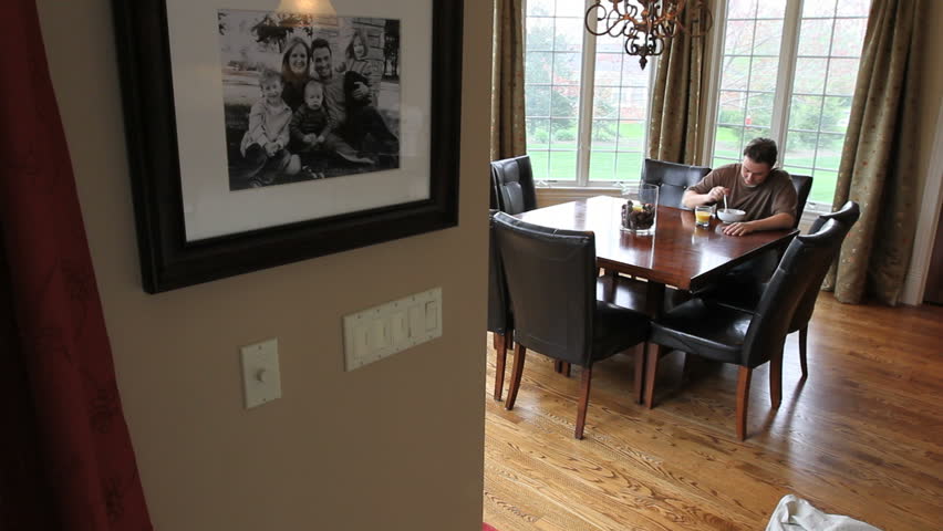 Moving dolly shot of a man eating breakfast by himself in the breakfast nook of a large luxury home