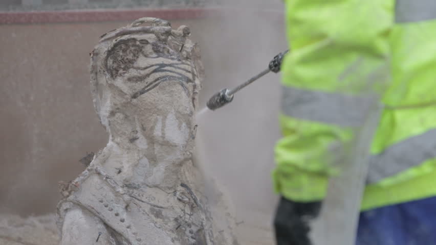Man using a water pressure hose to remove clay from a bronze statue