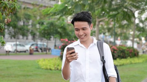 Happy Asian young student using mobile phone to online, texting, sms, outdoor green park.