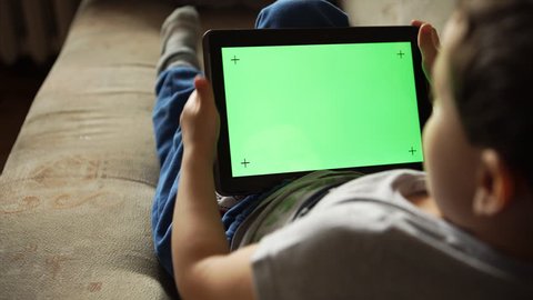 Child tilting to the left and right a tablet PC with green screen, back view
 Stock Video