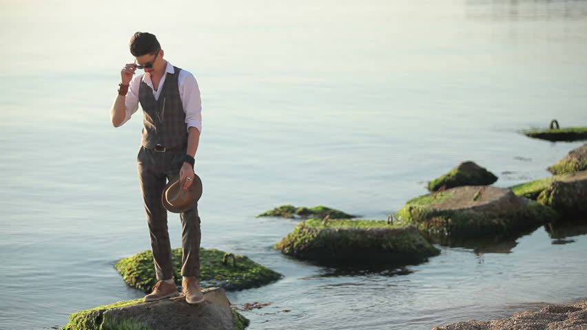 young man in suit and hat standing on a rock