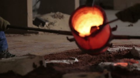 Workers in a bronze foundry pouring bronze into investments for a bronze statue
