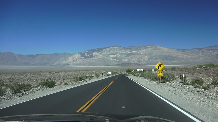 Driving through the California desert to Death Valley National Monument. Highway scenic landscapes of winding mountain roads an straight sloping long roads. Long views of volcanic terrain and plants.