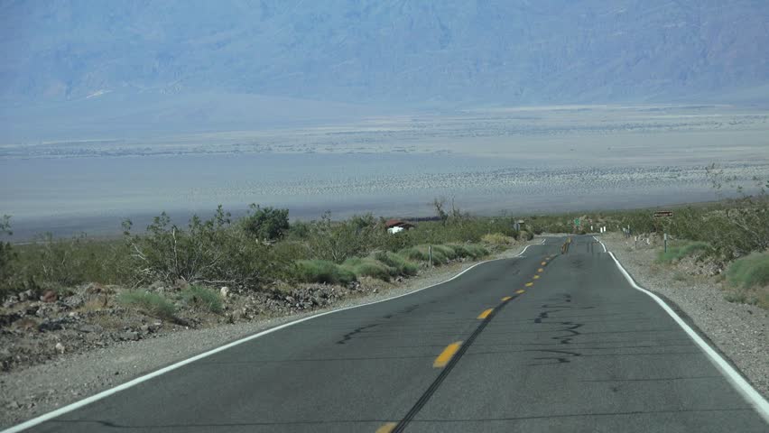 Driving through the California desert to Death Valley National Monument. Highway scenic landscapes of winding mountain roads an straight sloping long roads. Long views of volcanic terrain and plants.