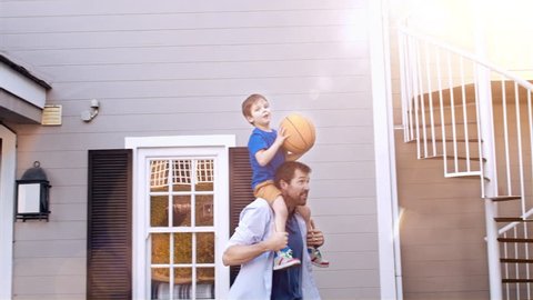 4k wide shot of father and son dunking the basketball in hoop on home driveway with sunflare. 