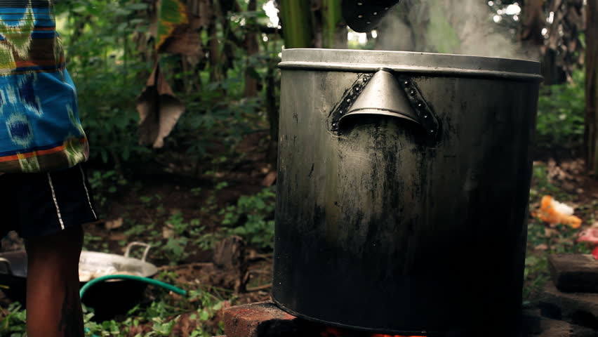 Big steel pot placed on open fireplace surrounded by jungle with green plants,