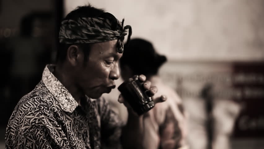 Man in traditional balinese clothing is drinking tee, shot with selective focus