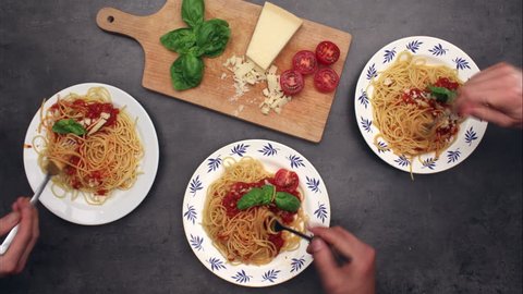 Serving and eating spaghetti with friends. Top view on dinning table with plates and cutting board with basil, tomatoes and parmesan. Time-lapse & stop motion, 4K