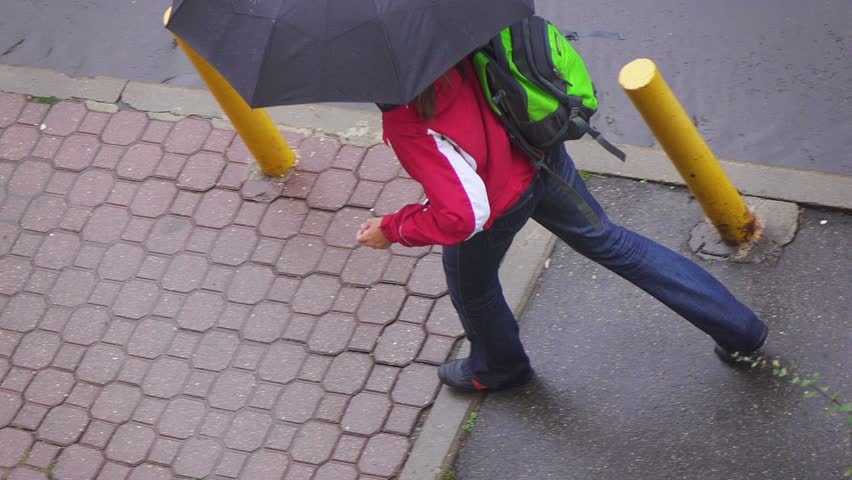 Rainy day in city streets, water drops, puddles, woman walking under umbrella, slow motion, overhead view.