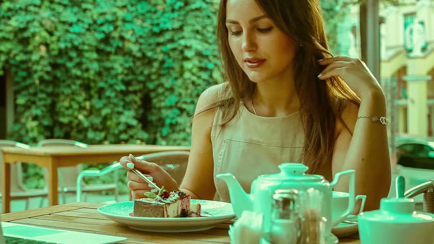 beautiful brunette eating delicious cheesecake in cafe outdoors