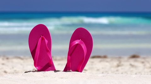 Pink flip flops on white sandy beach near sea waves, nobody. Summer vacation concept
