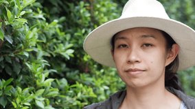 Video of Beautiful smiling Asian woman closeup portrait. Wearing hat with natural green bush background. modern life condominium