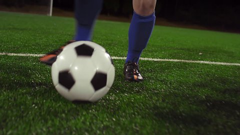 A female soccer player dribbles down the field at night while her opponents slide tackle and defend