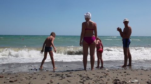 Parents and two children standing ankle deep in sea water, small wavesrolls