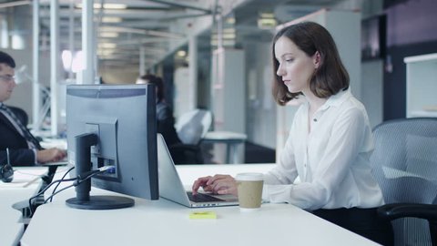 Female Office Worker is Working on Laptop and Drinking Coffee. Shot on RED Cinema Camera in 4K (UHD).