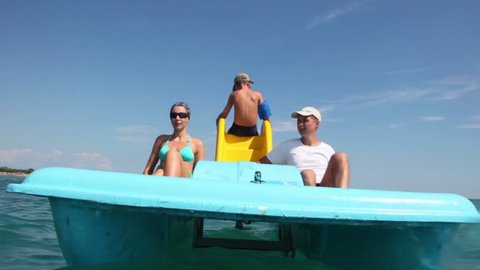Father, mother and their son sailing on catamaran, parents are rotating pedal and son sits back to camera