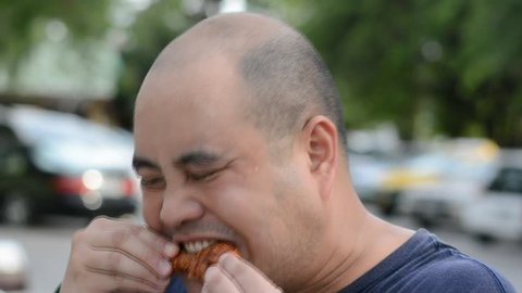 Fat Asian bald head Thai man is biting and eating fried chicken drumstick greedily with hunger with water sweat on his face in 1920x1080 HD quality. He might suffocate because of his gluttony.