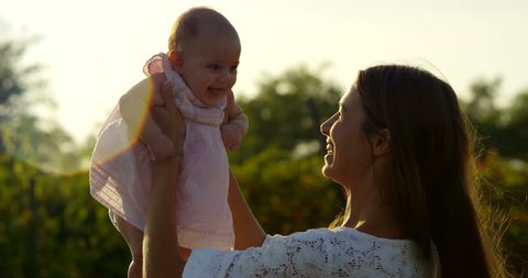 Super slow motion of young Caucasian mother and baby girl enjoy their happy moments together  in a meadow of vineyard on a sunshine in 4k (close up with flares)