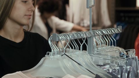 The girl chooses a blouse in a clothes store. Young teen girl in black t-shirt choosing a clothes on hangers in shop