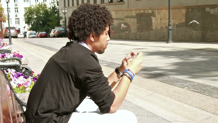 Young Man Sitting On The Bench And Texting Smartphone Device.