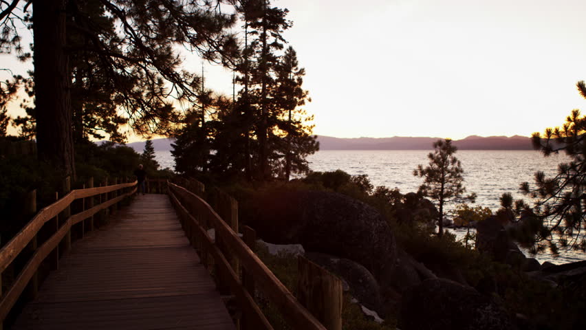 Static shot of a man walking on a path. Filmed at sunset on the boardwalk around the Sand Harbor overlook at Sand Harbor State Park, Lake Tahoe, Nevada.