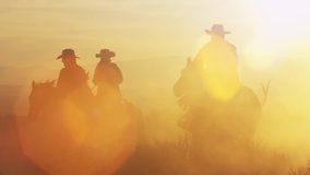Cowboys riding into the golden sunset at dusk with mountain range background, slow motion with strong sun lens flares. - Powered by Shutterstock - Get 15% off with code: PIKWIZARD15